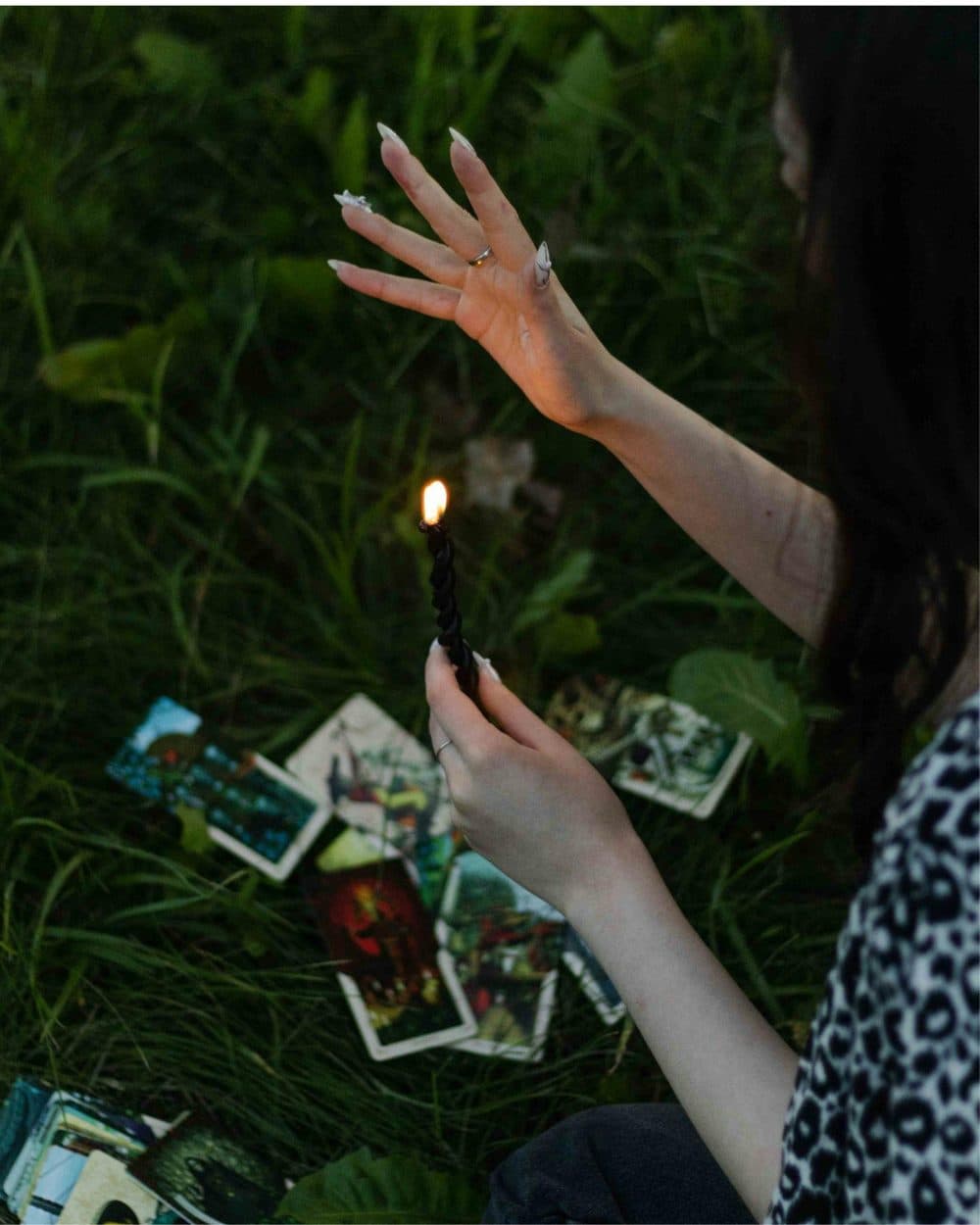 Manos sosteniendo una vela en una lectura de tarot sobre la hierba